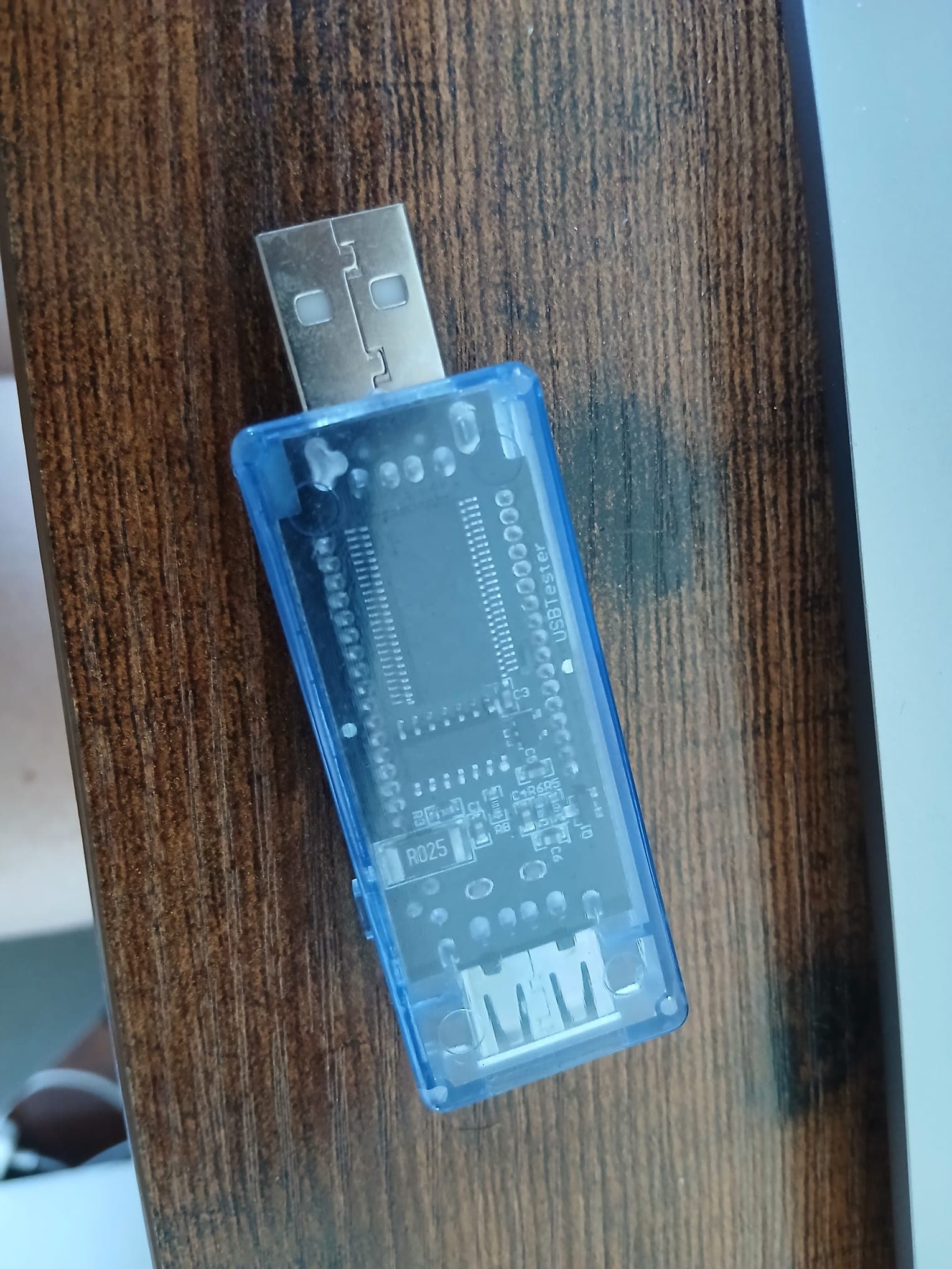 USB power meter with a translucent blue case, a male USB connector on one side and a micro-USB socket on the other.